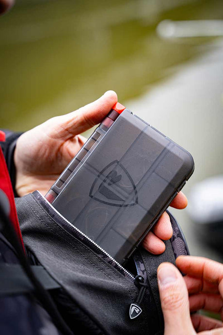 Caja de accesorios Fox Rage Mediana guardada en un bolsillo, ideal para organizar complementos de pesca.