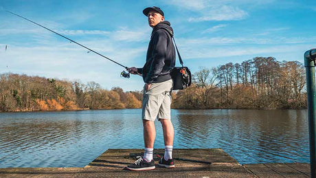 Hombre pescando en un lago, vistiendo pantalón corto Fox Rage Lightweight gris, ideal para la pesca.