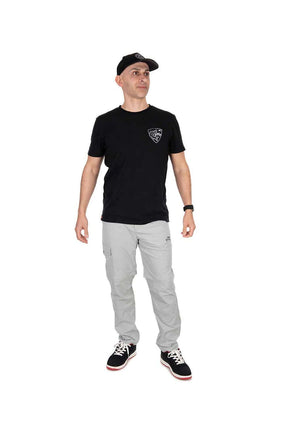 Hombre usando pantalón desmontable Fox Rage en gris claro, con camiseta negra y gorra, ideal para pesca al aire libre.