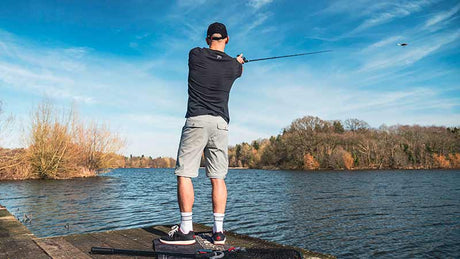 Hombre pescando en un lago con pantalón desmontable Fox Rage, disfrutando del aire libre en un día soleado.